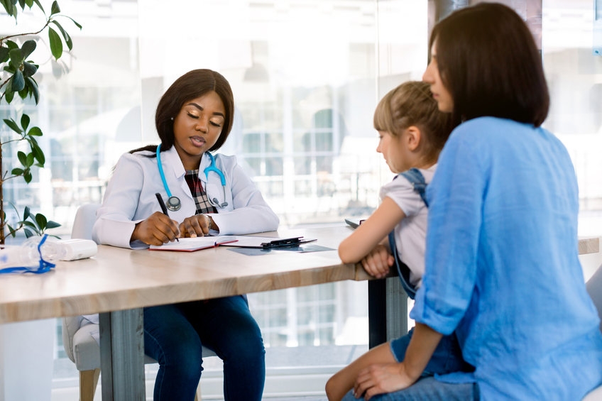 female dr writing prescription to young mother and child